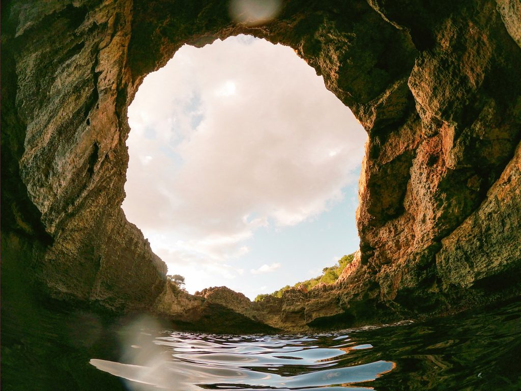 A nature photo taken from inside a cave, there's an imperfect circle opening to see the sky. This was chosen to represent boundaries for the blog post about capacity, boundaries and nervous system regulation.